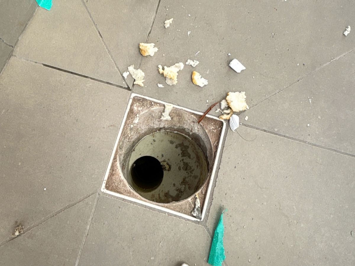 Ralo de piso com entulho de obra e tampa danificada